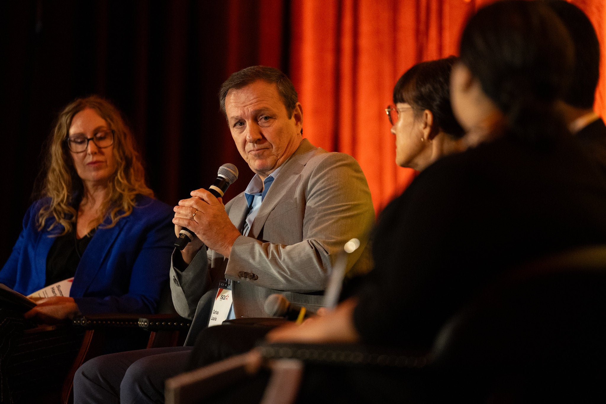 A man holds a microphone surrounded by other panelists in a conference.